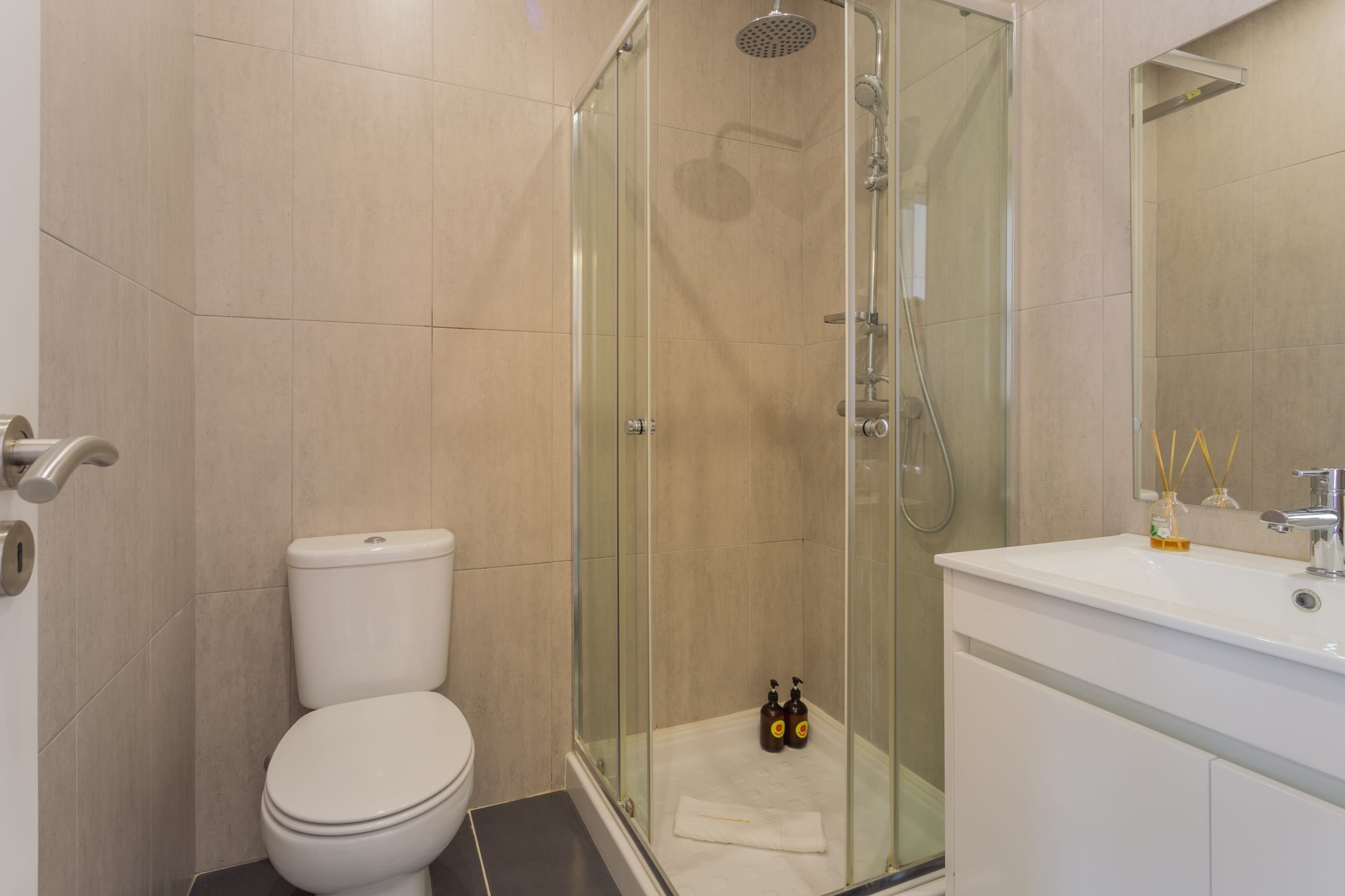 A modern bathroom with a glass-enclosed shower, a white toilet, and a sink with a mirror.