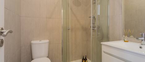 A modern bathroom with a glass-enclosed shower, a white toilet, and a sink with a mirror.