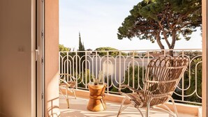 A balcony with wicker chairs and a wooden side table, overlooking a tree and a distant view. - Carla Rosa 11 Luxueux Studio Piscine - 1bdr (Cannes)