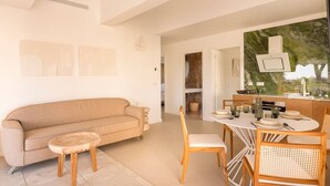 A modern living room with a beige sofa, a small round table, and a dining area with a white table and chairs. - Carla Rosa 10 Luxueux Appartement Piscine -2 BDR (Cannes)