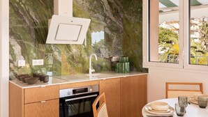 A modern kitchen with a marble backsplash, a built-in oven, and a window with a view of greenery. - Carla Rosa 10 Luxueux Appartement Piscine -2 BDR (Cannes)