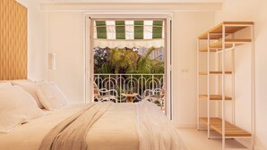 Quarto com cama, varanda com vista para palmeiras e estante de metal branca.
