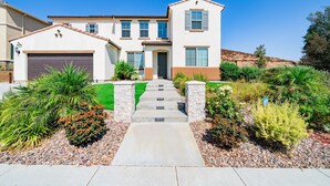 A two-story house with a garage, a front porch, and a landscaped garden with various plants and a stone pathway leading to the door. - Allura Champagne New in Wine Country Pool Game Rm (Winchester)
