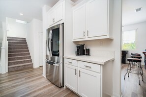 A modern kitchen with white cabinetry, a stainless steel refrigerator, and a coffee maker. - Allura Champagne New in Wine Country Pool Game Rm (Winchester)