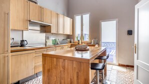 Eine Küche mit Holzausstattung, einer zentralen Kochinsel, Barhocker und Blick durch eine Glastür nach draußen.