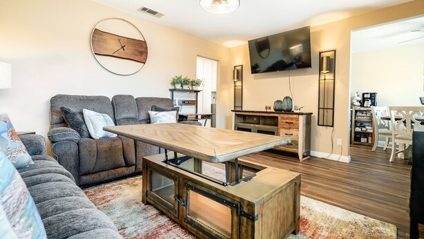 A modern living room with a sofa, a coffee table, a TV, and a dining area. - Lux - Charming San Marcos 2BR Patio Pet-friendly (San Marcos)
