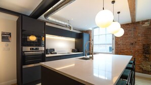 A modern kitchen with a large island, built-in appliances, and a brick wall.
