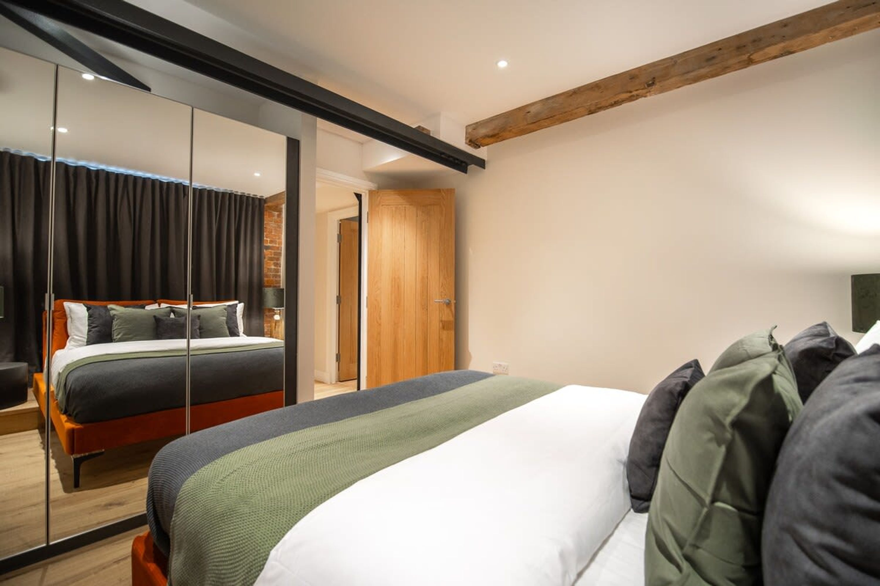 Quarto moderno com cama grande, espelho e viga de madeira no teto.