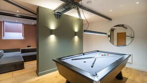 A pool table in a modern room with a wooden floor, a sofa, and a wall-mounted mirror.