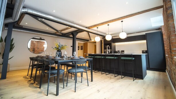 A modern kitchen with a central island, black bar stools, and a dining area with a round table and chairs.