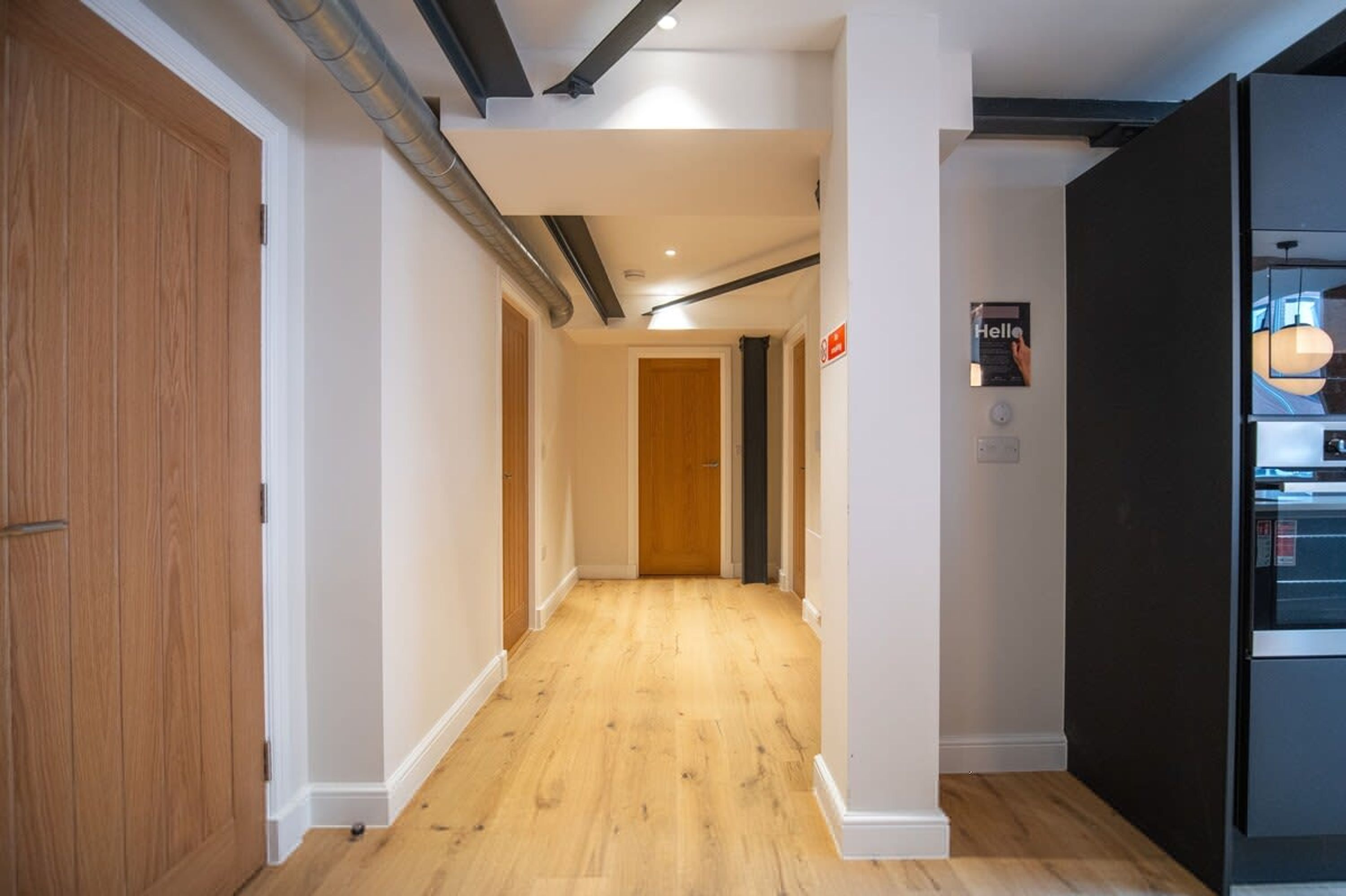 A hallway with wooden flooring, white walls, and a black refrigerator on the right.