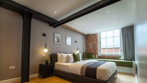 A modern bedroom with a large bed, a brick wall, and a window with curtains.