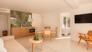 A modern living room with a sofa, a dining table with chairs, a kitchen area with a marble backsplash, and a TV mounted on the wall. - Carla Rosa 7 Appartement Moderne Piscine - 2 BDR (Cannes)