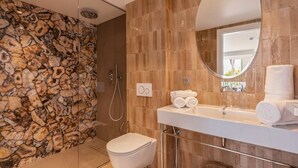 A modern bathroom with a stone wall, a round mirror, a white sink, and a toilet. - Carla Rosa 7 Appartement Moderne Piscine - 2 BDR (Cannes)