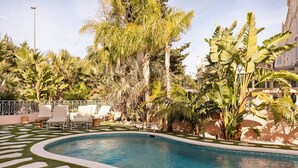 Une piscine entourée d’une végétation luxuriante et de palmiers, agrémentée de chaises longues et d’un chemin décoratif.