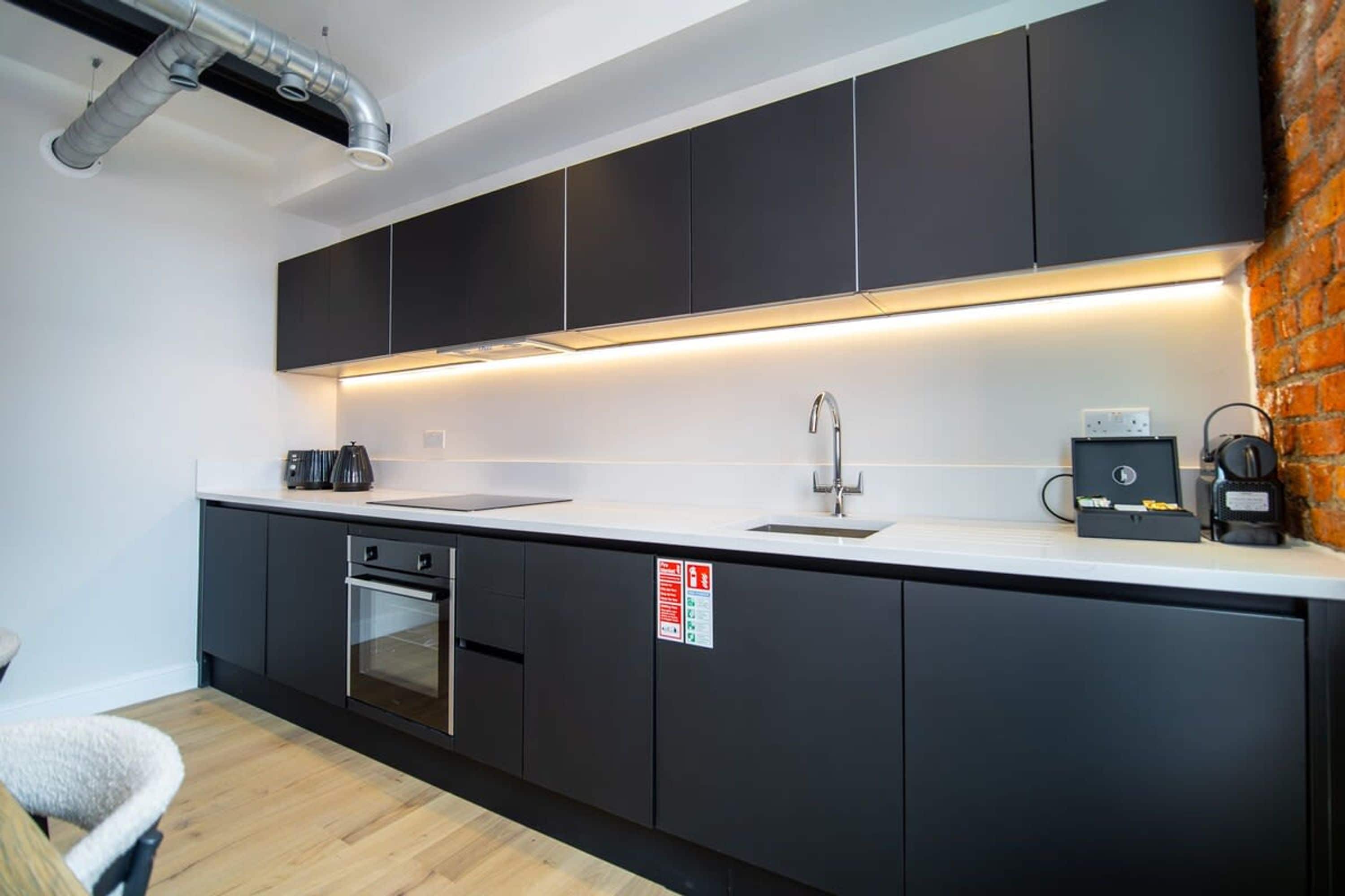 A modern kitchen with dark cabinets, a white countertop, stainless steel appliances, and a visible fire safety sign.
