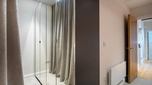 Un couloir avec une armoire à miroir, un radiateur et une porte en bois donnant sur une autre pièce.