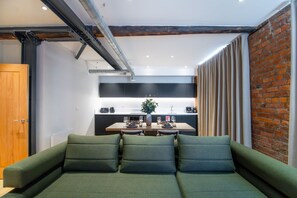 A modern living room with a green sofa, a dining area with a table set for two, and a brick wall.