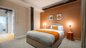 Une chambre moderne avec un grand lit, deux lampes fixées au mur et une porte donnant sur une autre pièce.