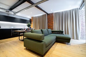 Uma sala de estar moderna com sofá seccional, área de jantar com mesa e cadeiras, e cozinha com armários pretos e parede de tijolos decorativa.