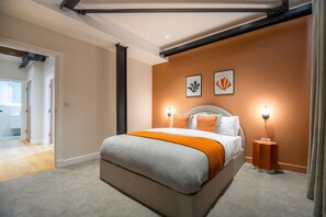 Une chambre moderne avec un grand lit, deux lampes fixées au mur et une porte donnant sur une autre pièce.