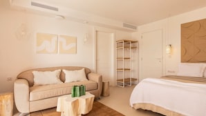 A modern bedroom with a beige sofa, a wooden coffee table, a bed with a white duvet, and a built-in shelving unit.