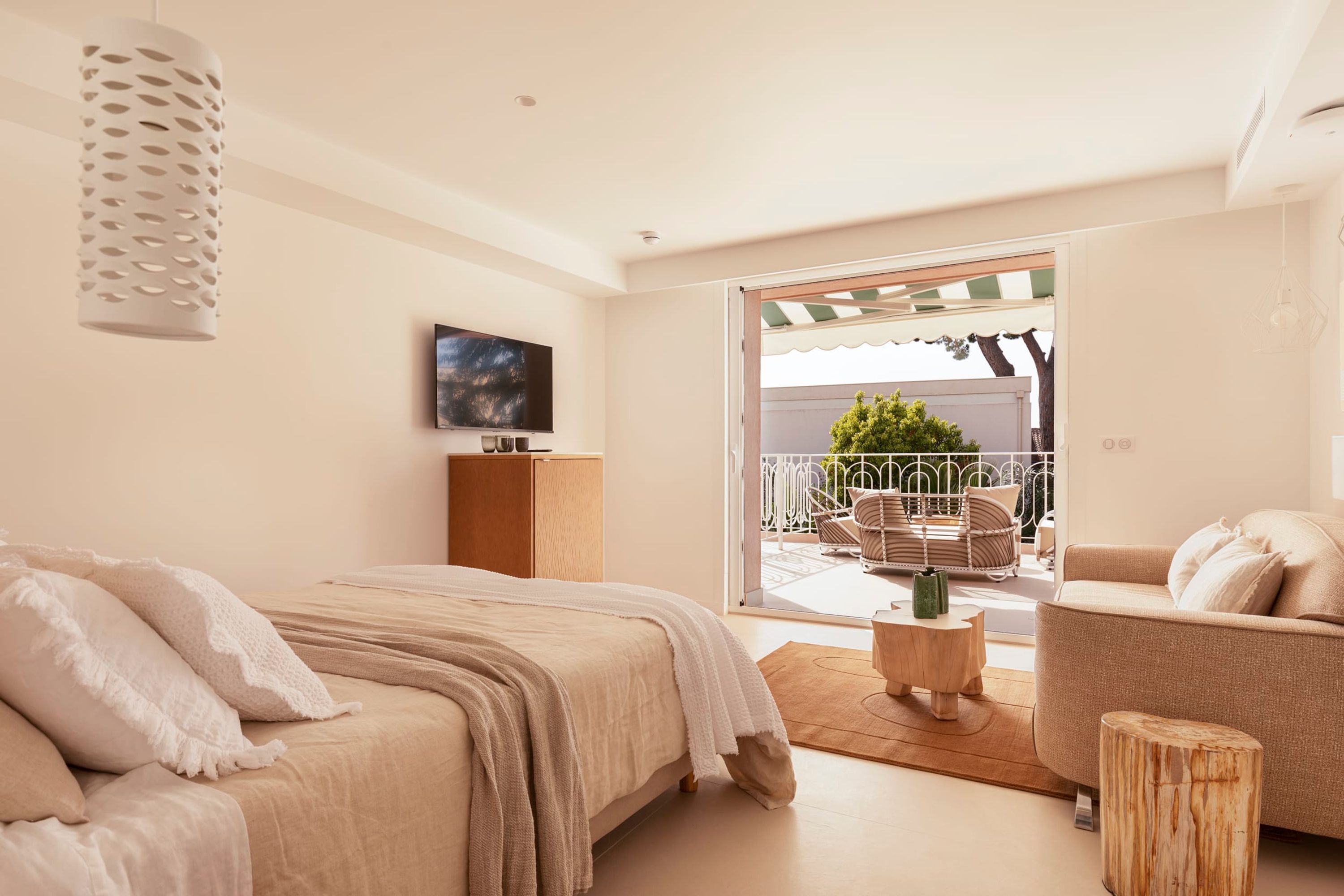 A modern bedroom with a bed, a wooden nightstand, a TV, and a balcony with outdoor furniture.