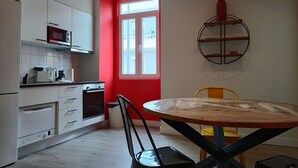 A modern kitchen with white cabinets, a red accent wall, a microwave, and a stove. There's a round table with chairs and a yellow chair in the dining area. - 1B Perfect for Families Nomads Near Gulbenkian (Lisbon)