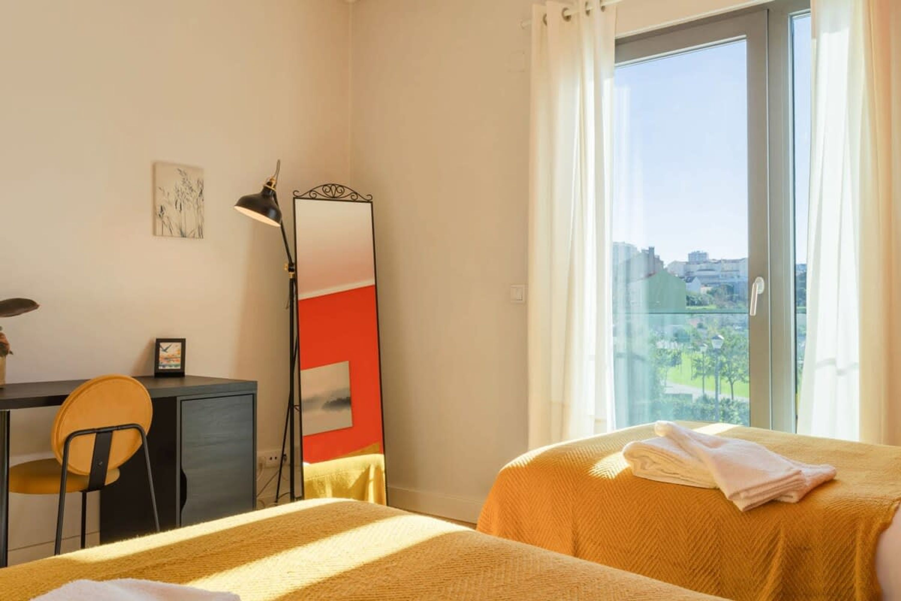 Une chambre d’hôtel équipée d’un lit, d’un bureau, d’une chaise, d’un grand miroir et d’une fenêtre donnant sur la ville.