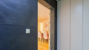 En modern hall med en mörk vägg och en dörr som leder till en matplats med mönstrade stolar.