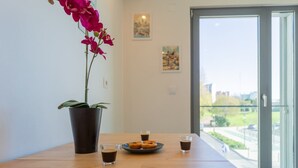 Ett bord med en orkidé i en kruka, en tallrik med munkar och fyra små glas kaffe i ett modernt rum med en glasdörr som leder ut till en utsikt över stadsbilden.