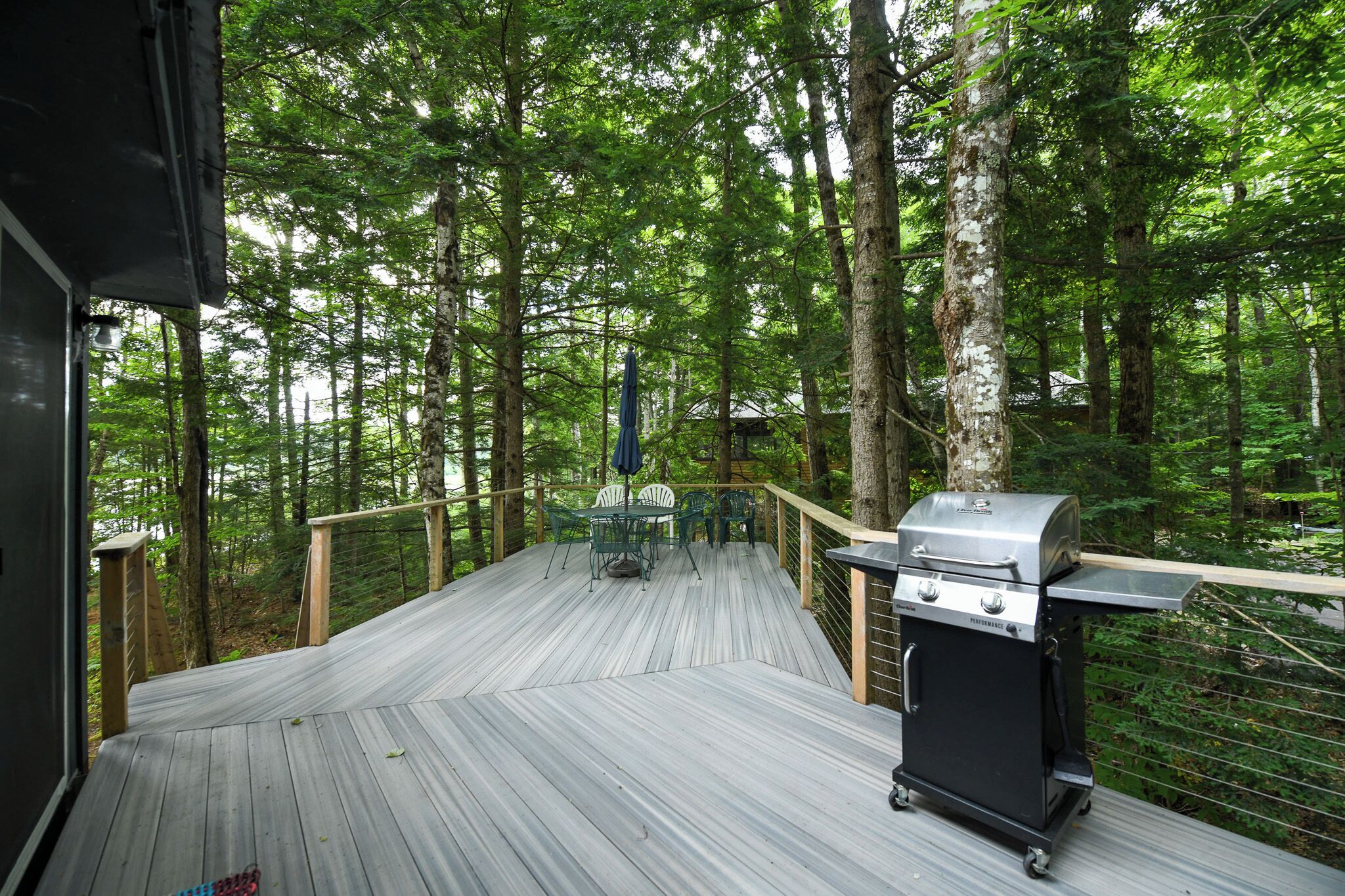A deck with a grill and chairs overlooking a forest.