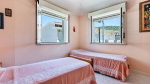 Un dormitorio con dos camas individuales, ventanas amplias y vistas a edificios.