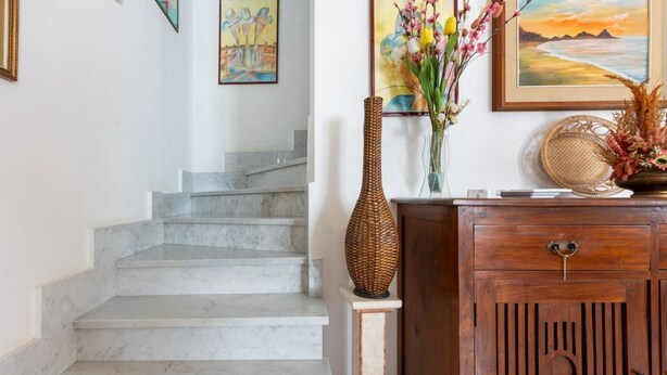 Una escalera con escalones de mármol, un armario de madera con una manija decorativa y un jarrón con flores sobre un pequeño pedestal.