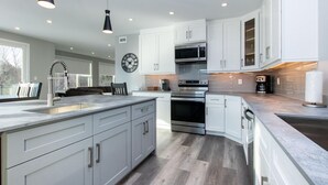 A modern kitchen with white cabinets, stainless steel appliances, and a large island. - High-tech Mountain Luxury Fitness Hot Tub BBQ (The Blue Mountains)