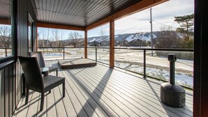 A covered outdoor deck with a view of a snowy landscape, a fireplace, and a seating area. - High-tech Mountain Luxury Fitness Hot Tub BBQ (The Blue Mountains)
