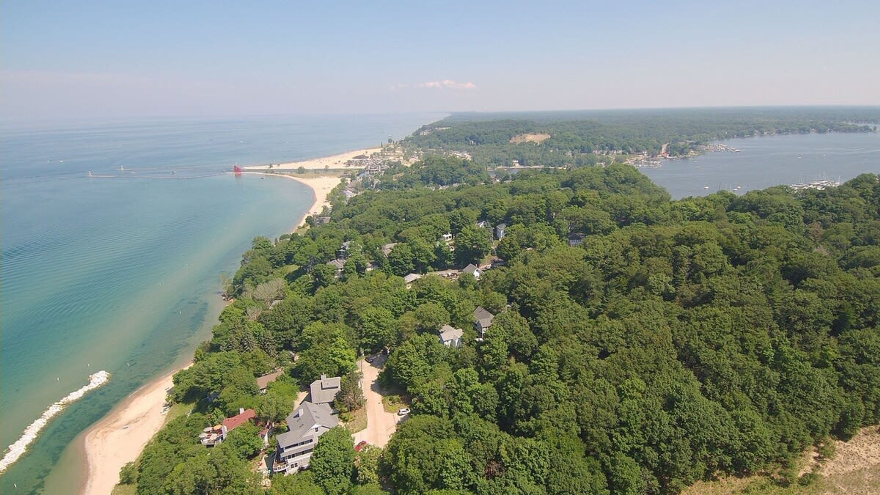 An aerial view of a coastal area with dense forest, a beach, and a lighthouse.