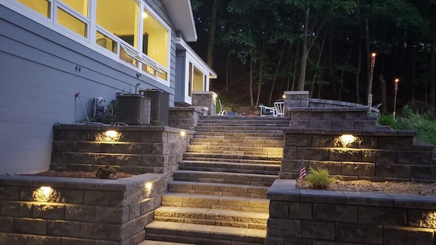 Un escalier en pierre menant à une maison, chaque marche étant agrémentée d’une petite lampe et un drapeau américain étant placé sur le côté droit.