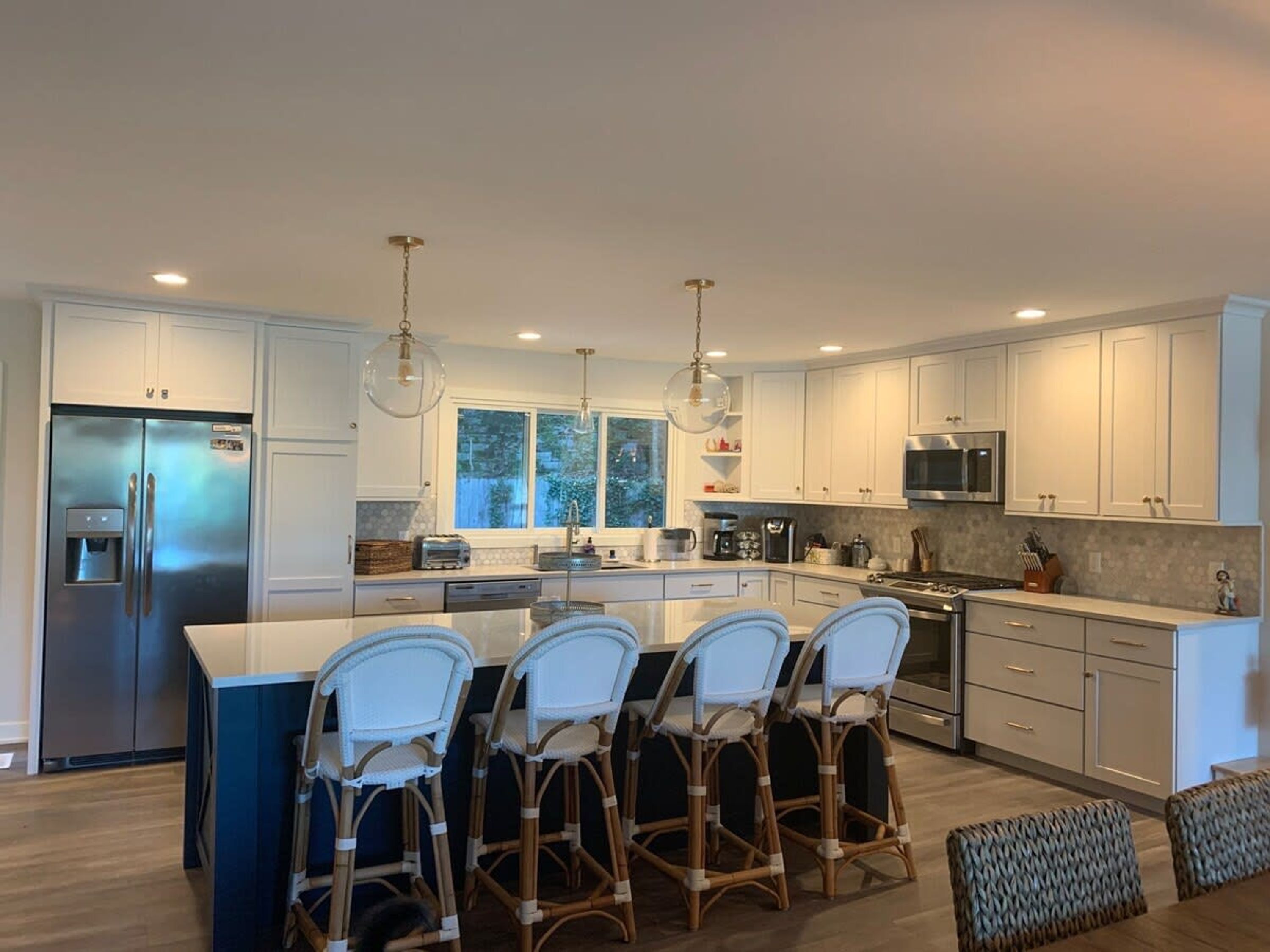 Una cocina moderna con armarios blancos, electrodomésticos de acero inoxidable y una isla central con taburetes de bar.