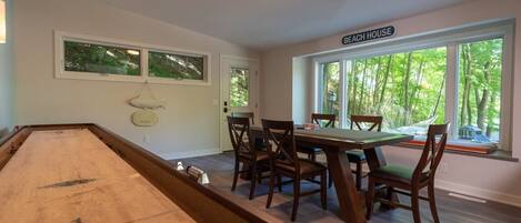 A pool table with chairs and a table in a room with large windows and a sign reading "Beach House".