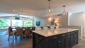 Une cuisine moderne dotée d’un grand îlot central, de meubles de rangement aux couleurs sombres et d’un éclairage suspendu.