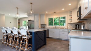 Une cuisine moderne avec des meubles blancs, un îlot central et un coin repas doté de chaises en osier.