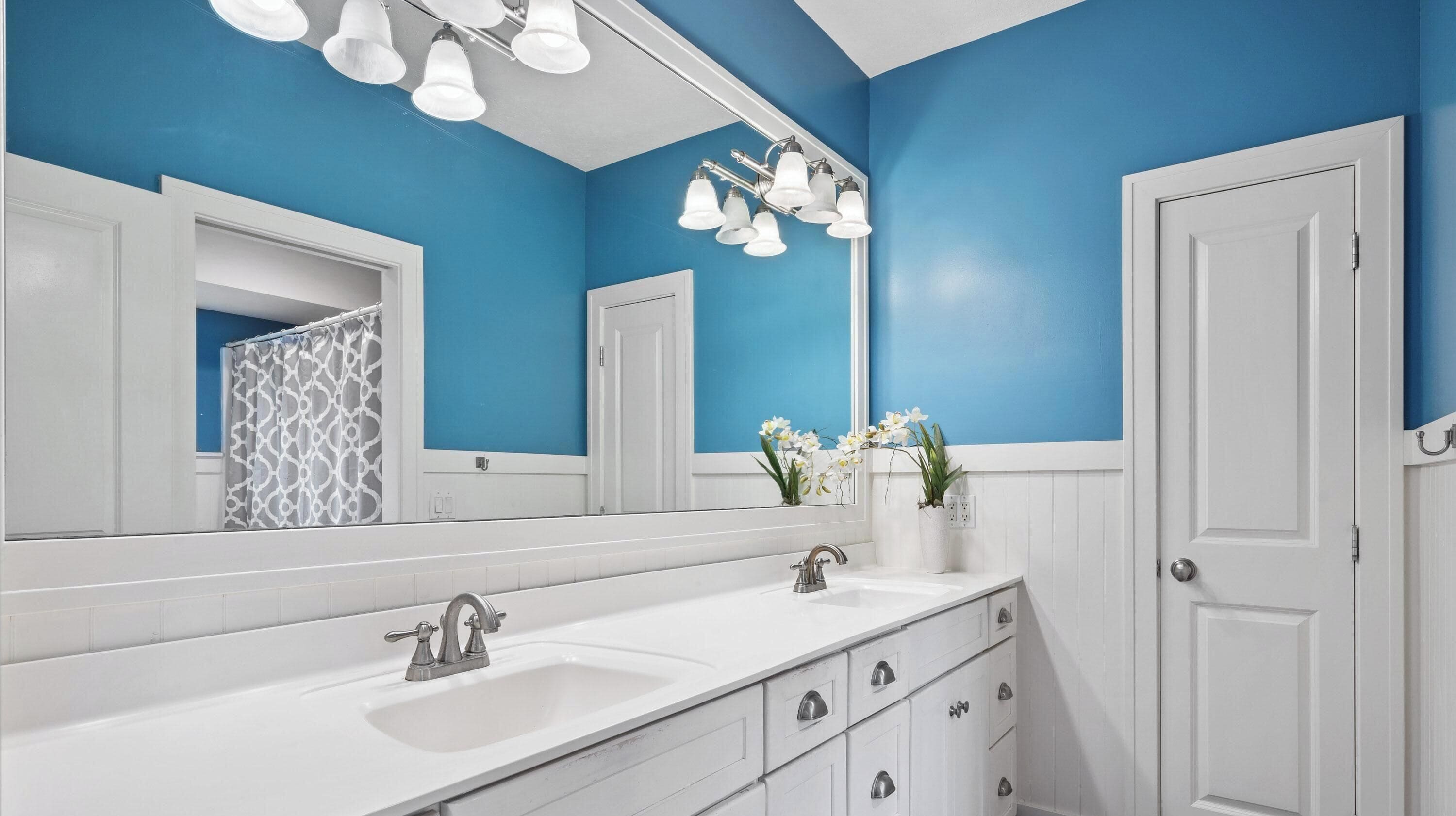 Une salle de bain avec un meuble-lavabo blanc, un grand miroir et un mur d’accent bleu.