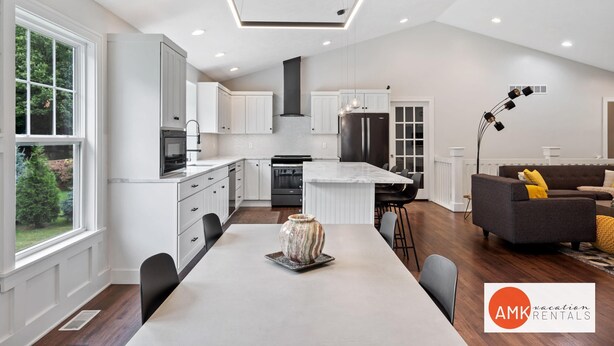 A modern kitchen with white cabinetry, a central island, and a dining area with a large table. - Destined for Relaxation (Saugatuck)