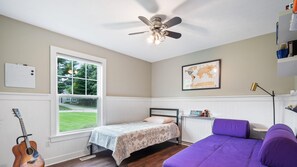 A bedroom with a bed, a guitar, a purple couch, a ceiling fan, a window with a view of a lawn, and a map on the wall. - Destined for Relaxation (Saugatuck)