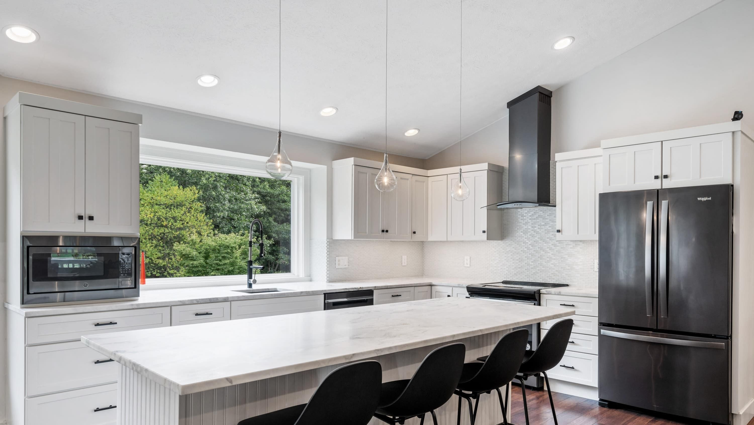 A modern kitchen with white cabinetry, a large island with bar stools, a stainless steel refrigerator, and pendant lighting.