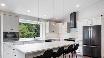 A modern kitchen with white cabinetry, a large island with bar stools, a stainless steel refrigerator, and pendant lighting.