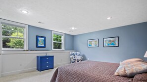 A bedroom with a large bed, a dresser, a chair, and two windows.
