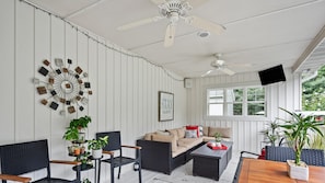 A cozy room with a sofa, chairs, a coffee table, and potted plants. There is a ceiling fan, a TV, and a window with a view of greenery. - Destined for Relaxation (Saugatuck)