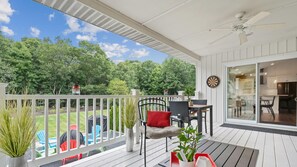 A covered outdoor deck with a dining area, a red tray with a plant, and a view of a lush garden.